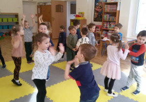 Widok na salę przedszkolną i grupę tańczących w parach dzieci.